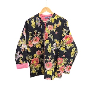 Puede incluir: Chaqueta acolchada negra con un vibrante estampado floral en tonos rosa, amarillo y verde. La chaqueta tiene forro y puños rosas. Cuelga de una percha de madera.