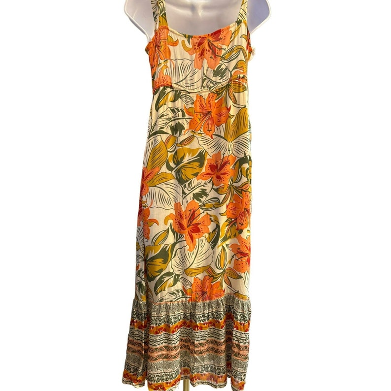 May include: A white maxi dress with a floral print featuring orange, red, and green flowers. The dress has a ruffled hem and a geometric pattern around the bottom.