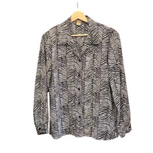 Könnte beinhalten: Ein schwarz-weiß gestreiftes Hemd mit Zebra-Muster, das an einem Holzbügel hängt. Das langärmlige Hemd hat einen Kragen und ein vertikales Streifenmuster. Das Hemd ist aus leichtem Stoff gefertigt.
