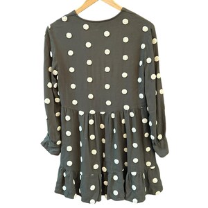 May include: A dark gray dress with long sleeves and a ruffled hem. The dress is adorned with white, textured polka dots. The dress is hanging on a wooden hanger.