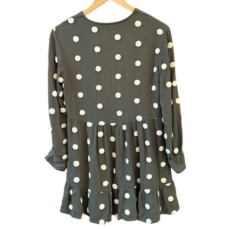 May include: A dark gray dress with long sleeves and a ruffled hem. The dress is adorned with white, textured polka dots. The dress is hanging on a wooden hanger.