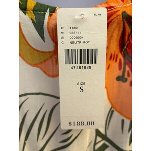 May include: A white tag with black text and a barcode. The tag says "C: 4130", "V: 022111", "S: 0000004", "C: NEUTR MOT", "47261888", "SIZE S", and "$188.00". The tag is attached to a white fabric with a floral print.