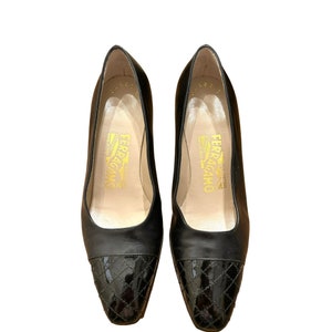 May include: A pair of black leather Salvatore Ferragamo pumps. The shoes feature a quilted design on the toe and a classic, elegant style. The interior of the shoe is a light tan colour with gold lettering.