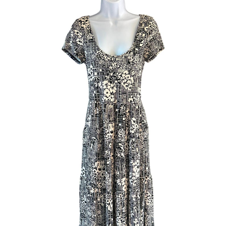 May include: A black and white floral print dress with a scoop neckline and short sleeves. The dress features a fitted bodice and a flowing, floor-length skirt. The pattern includes white flowers and geometric shapes.
