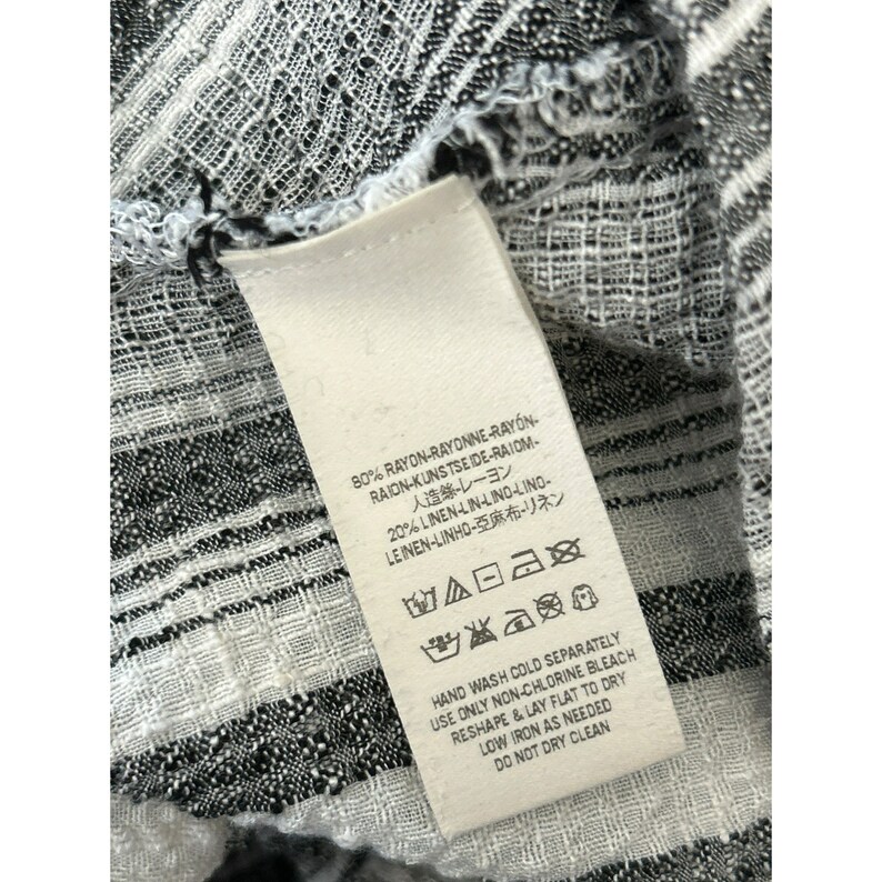 May include: White tag with black text and care instructions. The tag is attached to a black and white striped fabric. The text on the tag reads: 80% Rayon-Rayonne-Rayon-Raion-Kunstseide-Raiom-人造絲・レーヨン 20% Linen-Lin-Lino-Lino-Leinen-Linho-亞麻布・リネン Hand Wash Cold Separately Use Only Non-Chlorine Bleach Reshape & Lay Flat to Dry Low Iron As Needed Do Not Dry Clean