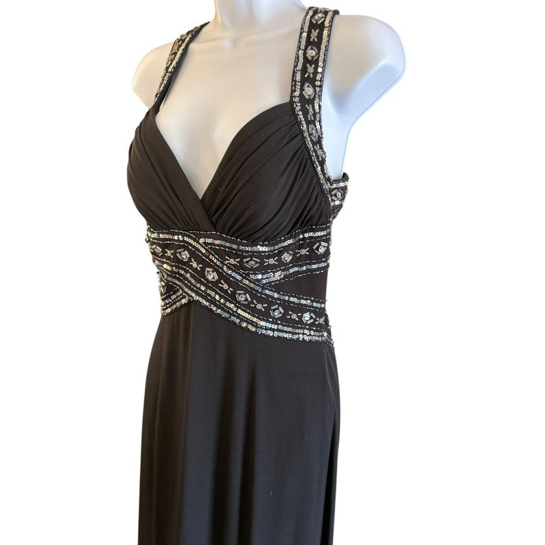 Puede incluir: Un vestido de noche negro de tirantes con escote pronunciado y un dise&ntilde;o de lentejuelas plateadas alrededor de la cintura.