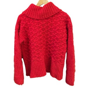 May include: A vibrant red sweater with a textured knit pattern and a wide, ribbed turtleneck. The sweater has long sleeves and a ribbed hem, displayed on a wooden hanger against a white background. The knitwear appears soft and warm.