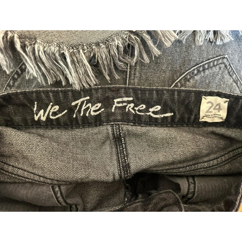 May include: A pair of black denim jeans with a frayed hem. The waistband has a black label with white text that reads "We The Free" and a size tag that says "24".