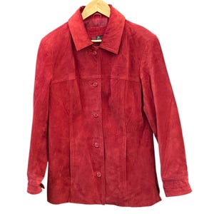May include: A red suede jacket with a collared neckline and button-down closure. The jacket is hanging on a wooden hanger against a white background. The jacket has long sleeves and a classic design.