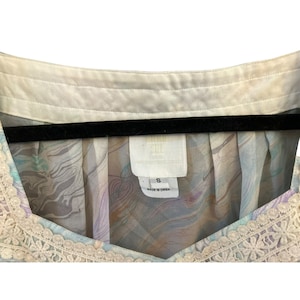 May include: A white and light blue patterned blouse with a lace trim. The blouse has a v-neck and is labeled "Rain Soul" with a size "S" and "Made in China".