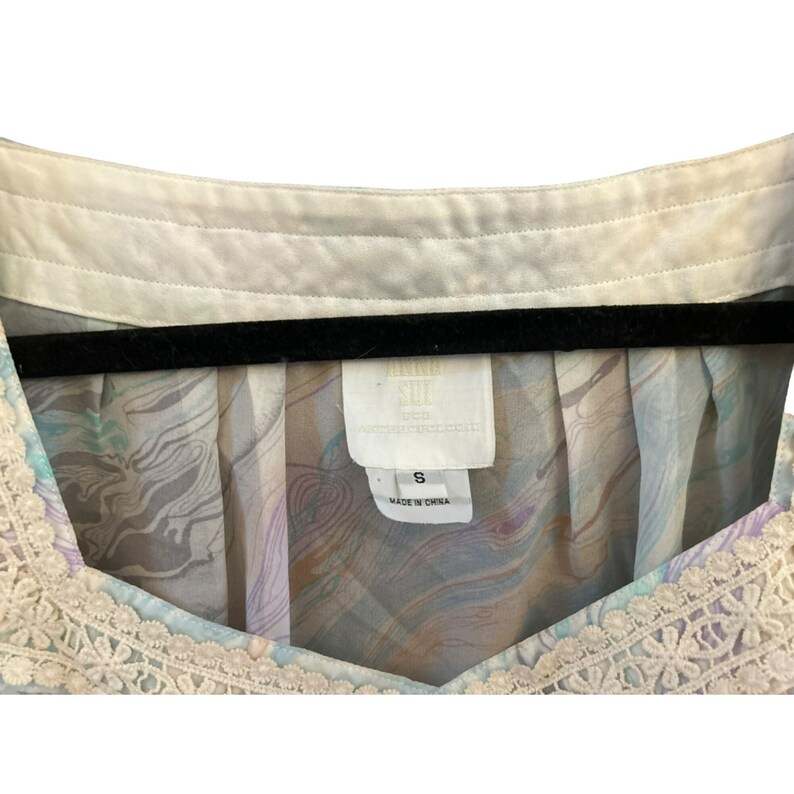 May include: A white and light blue patterned blouse with a lace trim. The blouse has a v-neck and is labeled "Rain Soul" with a size "S" and "Made in China".