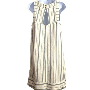 Puede incluir: Vestido blanco sin mangas con finas rayas negras y un escote en la espalda en forma de ojo de cerradura. El vestido tiene un dobladillo festoneado.