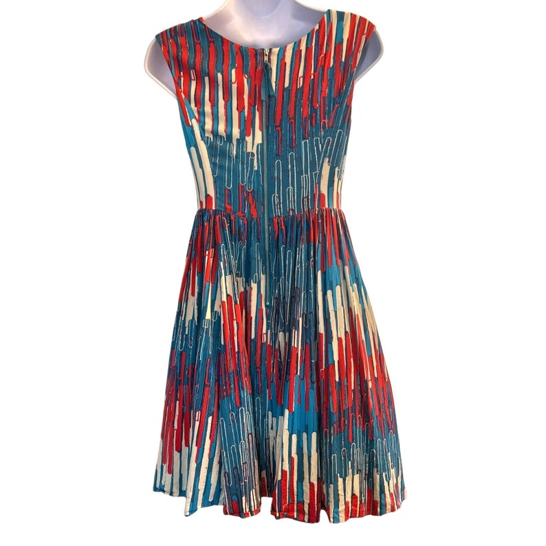 Op de afbeelding: Een mouwloze jurk met een abstract patroon in blauw, rood en wit. De jurk heeft een aansluitend bovenlijf en een volle rok.