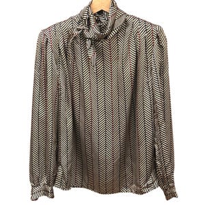 Könnte beinhalten: Eine langärmlige Bluse mit einem schwarz-weißen Fischgrätenmuster und roten vertikalen Streifen. Die Bluse hat eine Halsbinde und geknöpfte Manschetten. Das Kleidungsstück hängt an einem Holzbügel vor weißem Hintergrund.