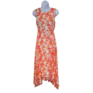 May include: Sleeveless dress with a floral pattern in shades of orange, pink, and white. The dress is knee-length and hangs on a white mannequin. The fabric appears lightweight and flowy, suitable for warm weather.