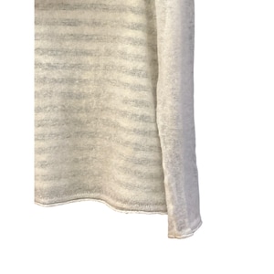 May include: Close-up of a light-colored, long-sleeved sweater. The sweater has a horizontal striped pattern in shades of white and gray. The fabric appears to be soft and slightly sheer, with a loose knit.