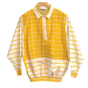 Peut inclure: Une chemise jaune et blanche à manches longues. Le devant présente un motif quadrillé, tandis que les manches sont rayées. Elle a un col blanc et trois boutons. Le bas de la chemise est doté d'une bande élastique jaune.