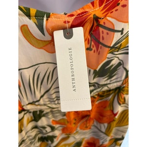 May include: A white dress with a floral print featuring orange, red, and yellow flowers. The dress has a tag that says "Anthropologie" on it.