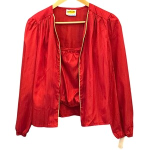 May include: A bright red long-sleeved jacket with a subtle vertical metallic pinstripe pattern. The jacket features a front opening with light-colored piping along the edges, gathered shoulders, and elasticized cuffs. A small white label is at the neck.