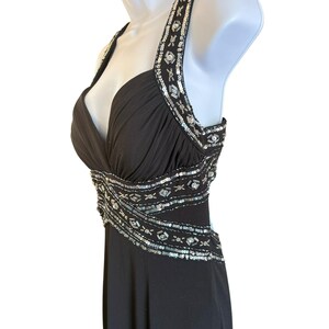 Puede incluir: Un vestido negro de tirantes con escote pronunciado y adornos de lentejuelas plateadas. El vestido tiene un corpi&ntilde;o ajustado y una falda fluida.