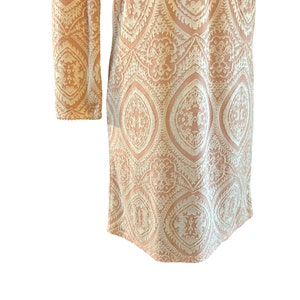Puede incluir: Un vestido largo de manga larga de color melocot&oacute;n con un estampado floral blanco intrincado.