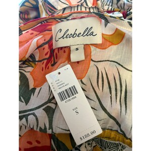 May include: A white, floral print dress with a ruffled neckline. The dress has a tag that says "Cleobella" and "S" for size. The tag also has a barcode and the price of $188.00.