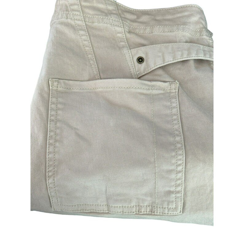 May include: A pair of beige cargo pants with a large patch pocket on the right side. The pocket has a stitched edge and is sewn onto the pants.