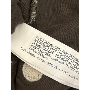 May include: Close-up of a clothing tag with text in multiple languages, including English, Spanish, and Japanese. The tag is attached to a brown fabric with white polka dots. The tag reads "100% viscose".
