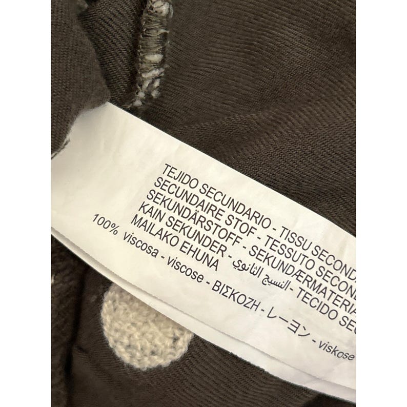 May include: Close-up of a clothing tag with text in multiple languages, including English, Spanish, and Japanese. The tag is attached to a brown fabric with white polka dots. The tag reads "100% viscose".