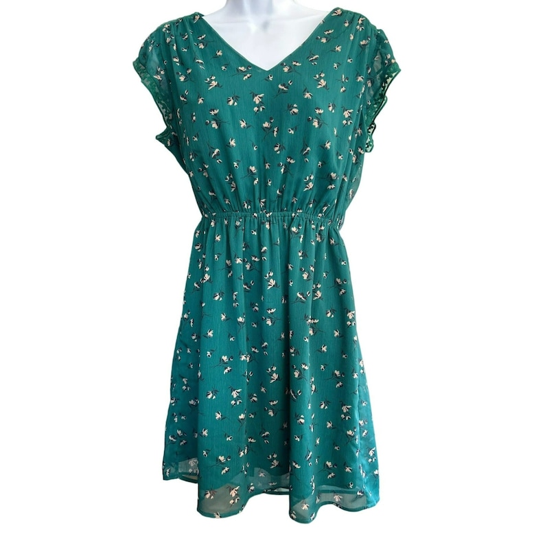 May include: A green floral print dress with a v-neck and short sleeves. The dress has a fitted bodice and a flowy skirt.