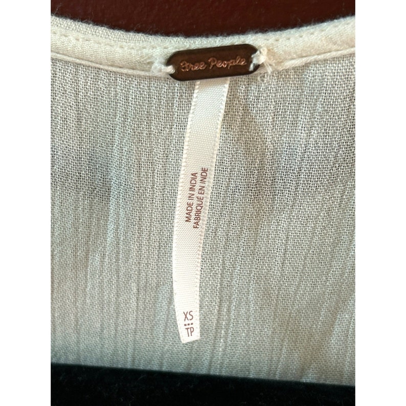 May include: White Free People brand clothing tag with the text "Made in India Fabrique en Inde" and "XS TP" printed on it.