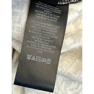 May include: A black clothing tag with white text detailing washing instructions. The tag includes information on machine washing cold, using non-chlorine bleach, reshaping, and low-temperature ironing. The tag also has a series of laundry symbols.