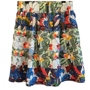 Puede incluir: Una falda de estampado floral colorido con cierre de cremallera. La falda tiene un estampado azul, verde, rojo y amarillo con una variedad de flores y hojas.