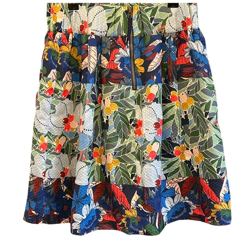 Puede incluir: Una falda de estampado floral colorido con cierre de cremallera. La falda tiene un estampado azul, verde, rojo y amarillo con una variedad de flores y hojas.
