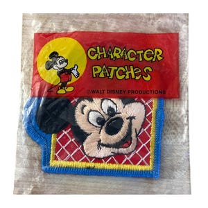 May include: A rectangular embroidered patch featuring a close-up of Mickey Mouse's face on a red and white grid background with a blue border. The packaging header is red with the text CHARACTER PATCHES and WALT DISNEY PRODUCTIONS.