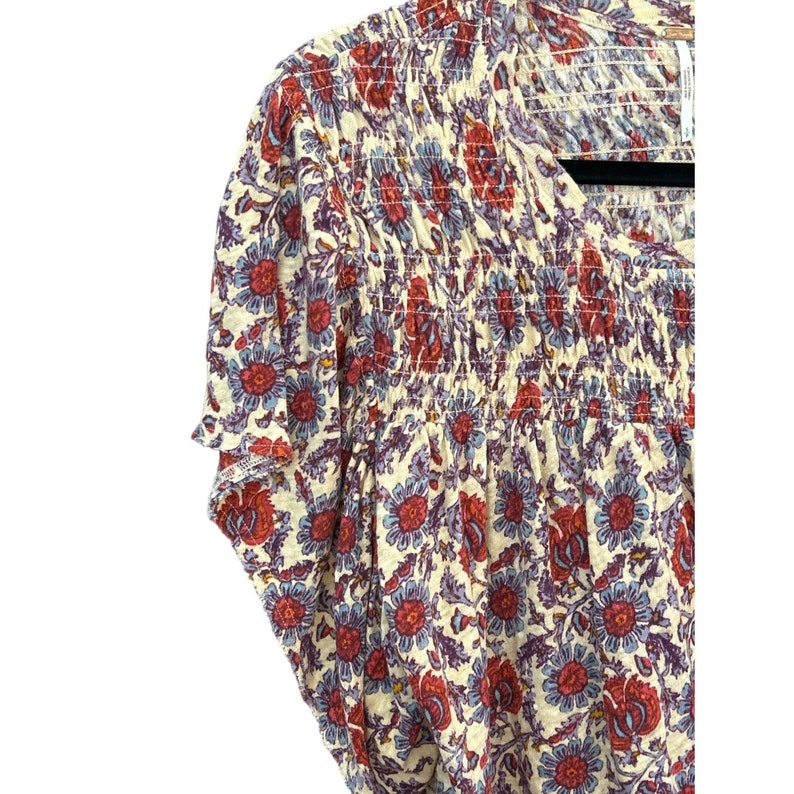 Peut inclure: Un chemisier &agrave; manches courtes de couleur cr&egrave;me avec un imprim&eacute; floral dans les tons de rouge, bleu et violet. Le chemisier a un col fronc&eacute; et une coupe ample.