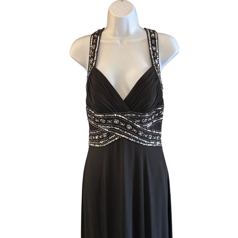 Puede incluir: Un vestido negro de maxi largo con un corpi&ntilde;o de lentejuelas plateadas. El vestido tiene un escote en V y una falda fluida.