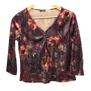 May include: A long-sleeved, V-neck top with a floral pattern in shades of burgundy, gold, and green. The top has a ruched detail at the bust and the tag reads "California Concepts". The fabric appears to be a soft velvet.