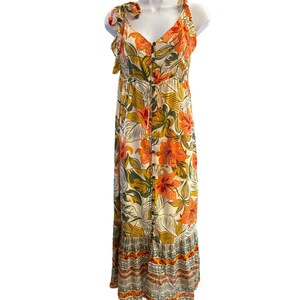 May include: A long, white maxi dress with a floral print in shades of orange, green, and yellow. The dress has a button-up front, a tie at the waist, and a tiered skirt.