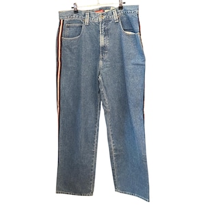 May include: Blue denim jeans featuring a straight-leg cut and a high-rise waist. The sides of the legs are accented with a vertical stripe in white, red, and dark blue. The jeans include a standard button fly closure, belt loops, and pockets.