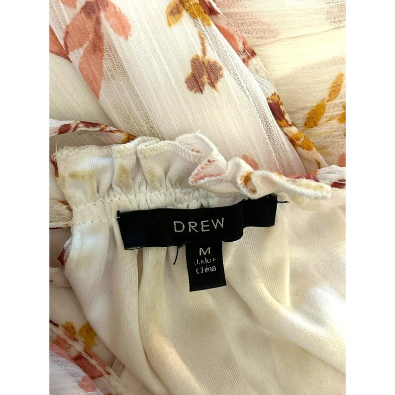 Pode incluir: Vestido branco com estampa floral, decote com babados e uma etiqueta preta que diz "DREW" e "M feito na China".