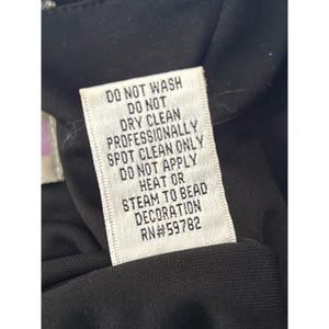 Puede incluir: Etiqueta de cuidado blanca con texto negro que dice "NO LAVAR, NO LIMPIAR EN SECO, LIMPIAR EN SECO PROFESIONALMENTE, NO APLICAR CALOR O VAPOR A LA DECORACI&Oacute;N DE PERLAS, RN#59782".