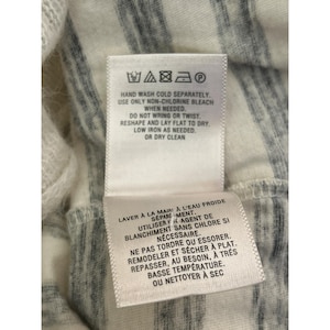 May include: Close-up of a white and gray striped fabric with two care instruction labels attached. The labels provide washing and drying instructions, including hand washing, non-chlorine bleach, and low iron.