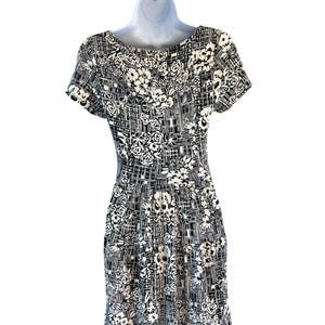 May include: A black and white patterned dress with a floral and geometric design. The dress features short sleeves and a fitted bodice that flows into a pleated skirt. The pattern includes roses and grid-like shapes.