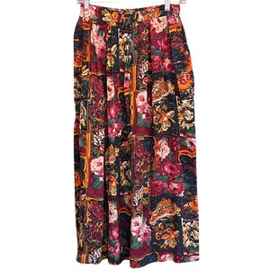 Puede incluir: Falda larga con estampado floral y diseño patchwork. La falda presenta una variedad de estampados florales en tonos rojos, rosas, amarillos y verdes sobre un fondo azul oscuro. La falda está colgada en una percha de metal.