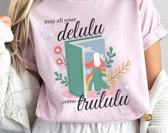 May include: Pink t-shirt with a graphic of a book with a woman stepping out of it. The text on the shirt reads "may all your delulu come trululu".