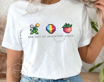 May include: White t-shirt with a pixelated graphic of a flower, a rainbow ball, and a red fruit. The text "BRB OUT OF INVENTORY SPACE" is printed below the graphic.