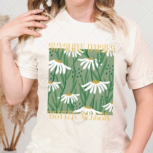 May include: A white t-shirt with a green and white floral design and the text "Sunshine Daisies & Butter Melons" in gold lettering.