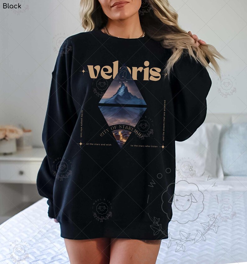 Puede incluir: Sudadera negra con un dise&ntilde;o gr&aacute;fico que presenta una cordillera y el texto "velaris city of starlight" en una fuente dorada.