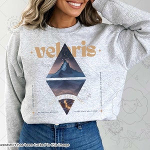 Puede incluir: Una sudadera gris con un dise&ntilde;o gr&aacute;fico de una cordillera monta&ntilde;osa y la palabra "velaris" en una fuente marr&oacute;n. El texto "to the people who took at the stars and wish to the stars who listen and the dreams that are answered" tambi&eacute;n est&aacute; impreso en la sudadera.